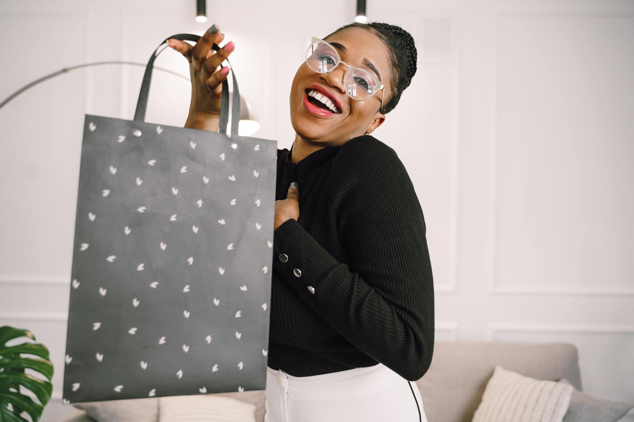 Joyful woman with eyeglasses holding a shopping bag in a modern room.